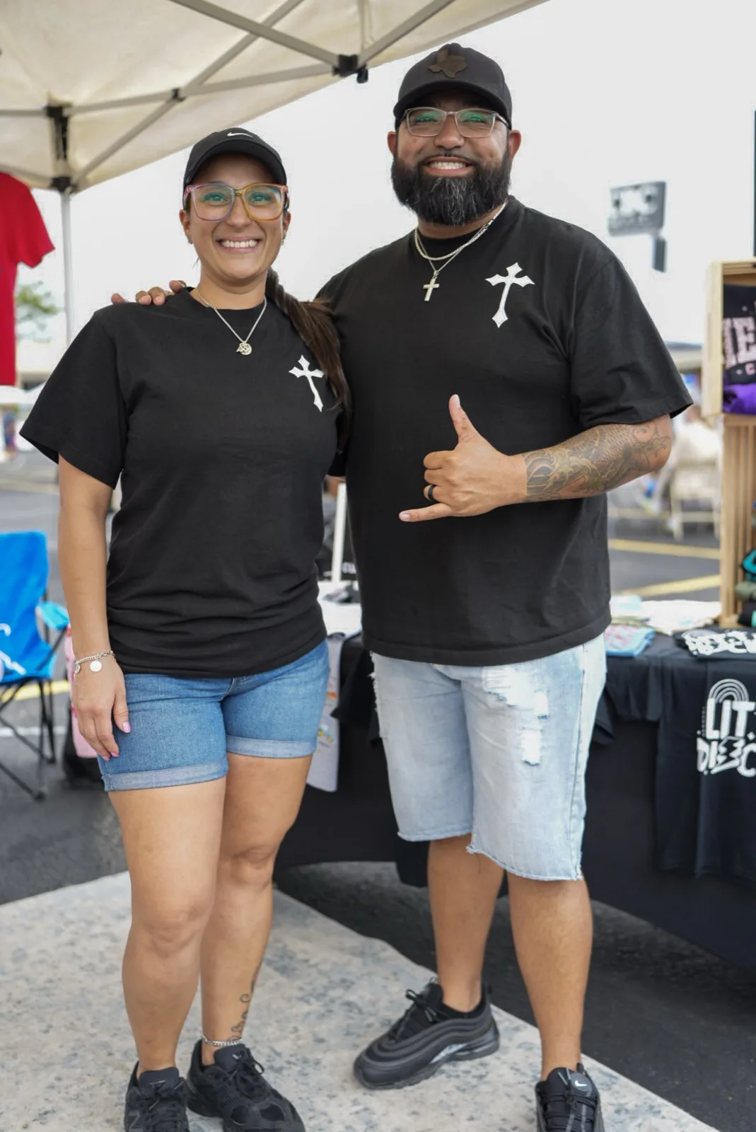 A vendor couple in matching black cross t-shirts smiling behind their booth at Holy City Market.