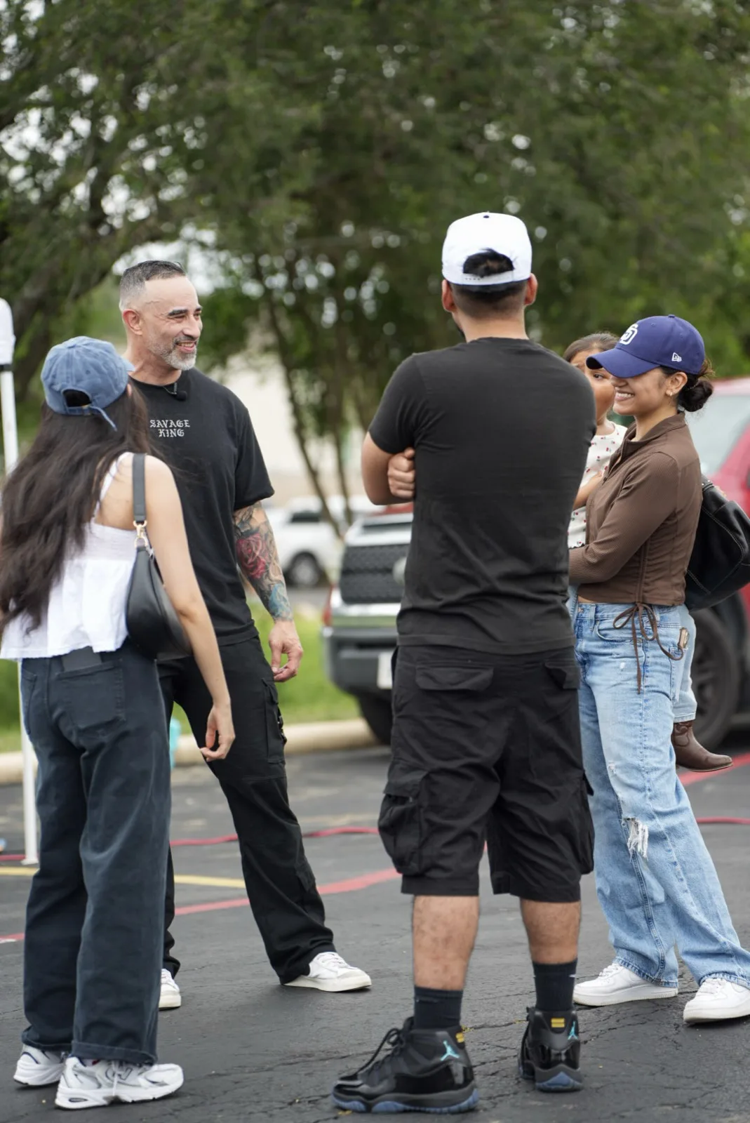 Groups of attendees chatting in the parking lot at Holy City Market with vendor tents in the background.