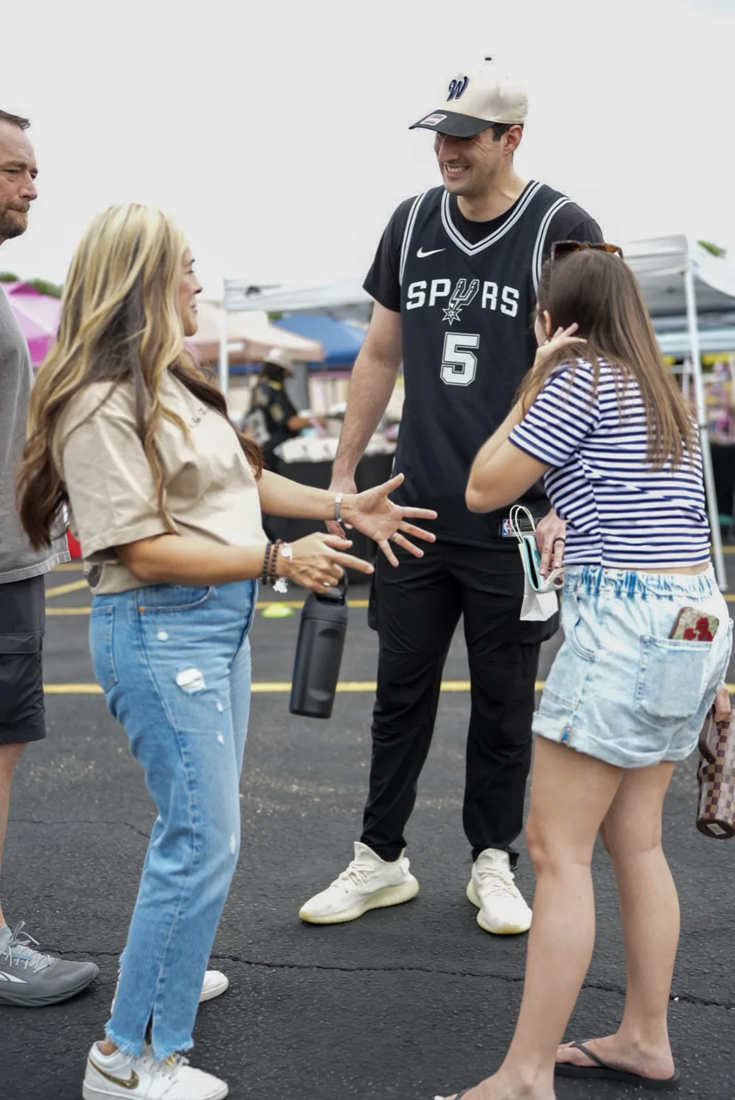 A man in a Spurs jersey greets a woman and young girl in the market aisle.